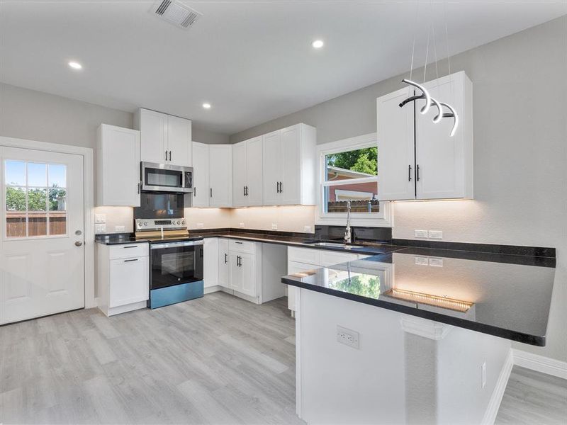 Kitchen with stainless steel appliances, a sink, a peninsula, light wood-style flooring, and white cabinetry Kitchen with stainless steel appliances, a sink, a peninsula, light wood-style flooring, and white cabinetry