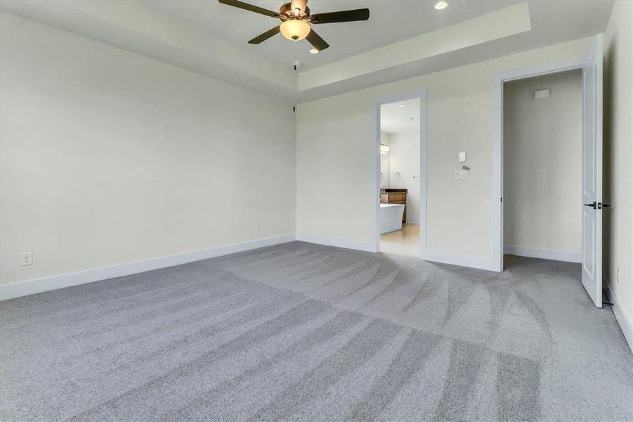 Spacious room featuring light gray carpeting, neutral wall finishes, and a tray ceiling with recessed lighting Spacious room featuring light gray carpeting, neutral wall finishes, and a tray ceiling with recessed lighting