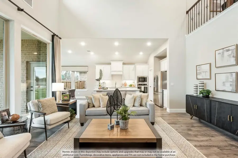 Open-concept living room with high ceilings, hardwood floors, and white kitchen visible in background
