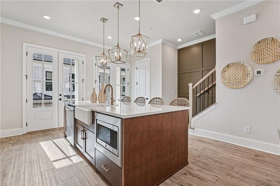 Kitchen with decorative light fixtures, light wood-type flooring, ornamental molding, stainless steel appliances, and light stone counters