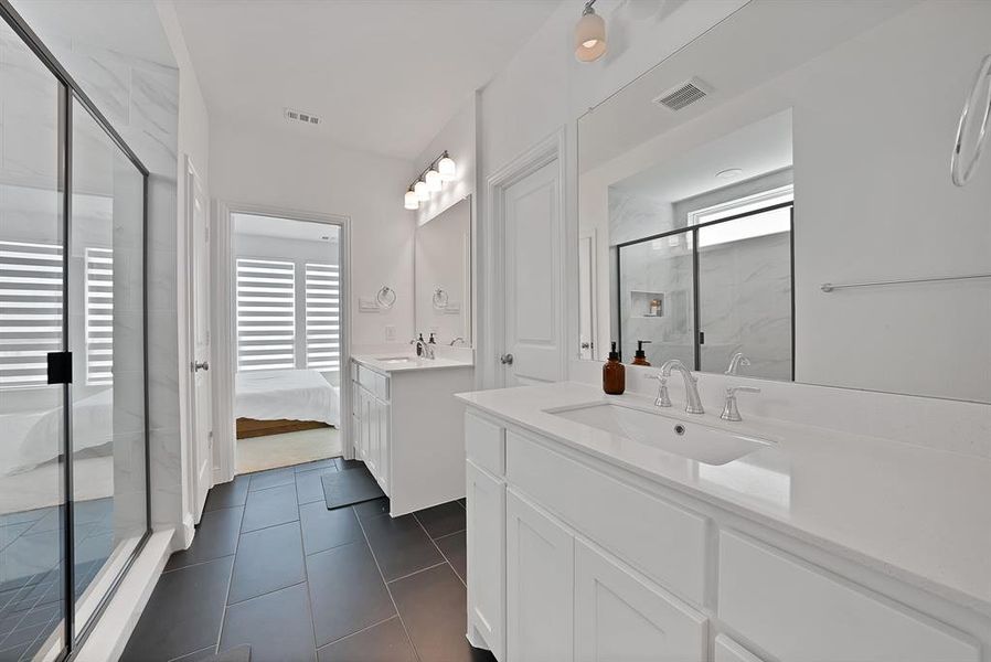 Dual vanity bathroom featuring stone countertops, integrated sinks, white cabinetry, and matte black tile flooring