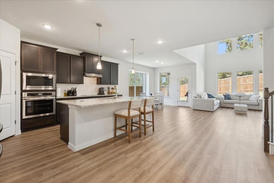 Kitchen with appliances with stainless steel finishes, light wood-type flooring, dark brown cabinets, decorative light fixtures, and an island with sink