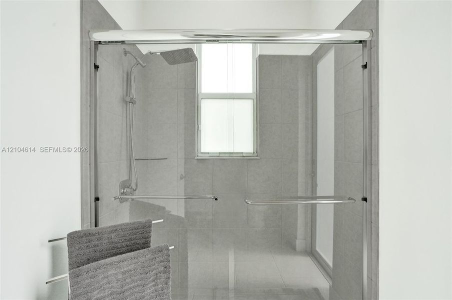 Frameless glass shower enclosure featuring a rainfall showerhead and integrated window