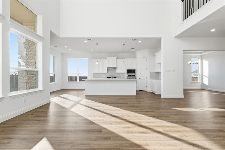 Unfurnished living room featuring a high ceiling, healthy amount of natural light, hanging lights, and dark wood-type flooring Unfurnished living room featuring a high ceiling, healthy amount of natural light, hanging lights, and dark wood-type flooring