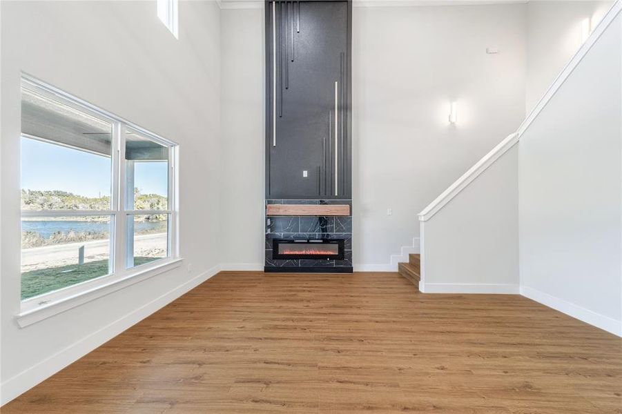Unfurnished living room featuring a high ceiling, light wood-style floors, a fireplace, stairway, and a water view Unfurnished living room featuring a high ceiling, light wood-style floors, a fireplace, stairway, and a water view