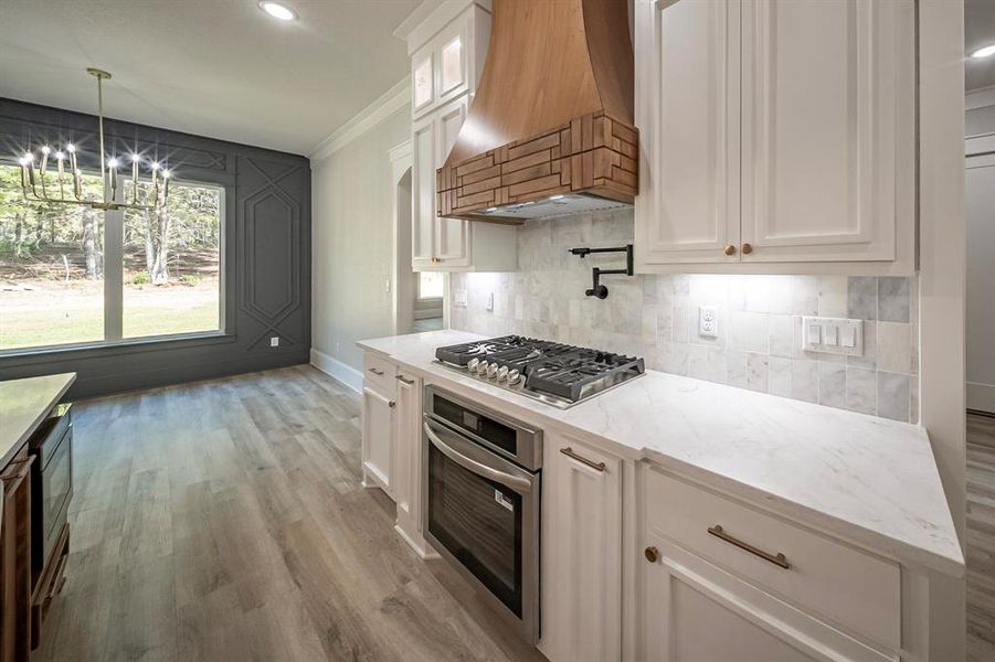 Kitchen featuring crown molding, decorative light fixtures, white cabinetry, appliances with stainless steel finishes, and dark wood-style flooring Kitchen featuring crown molding, decorative light fixtures, white cabinetry, appliances with stainless steel finishes, and dark wood-style flooring