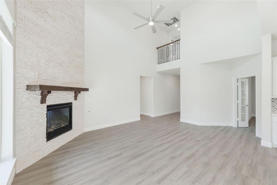 Open living room with two-story ceiling, stone fireplace, wood mantel, and light hardwood floors