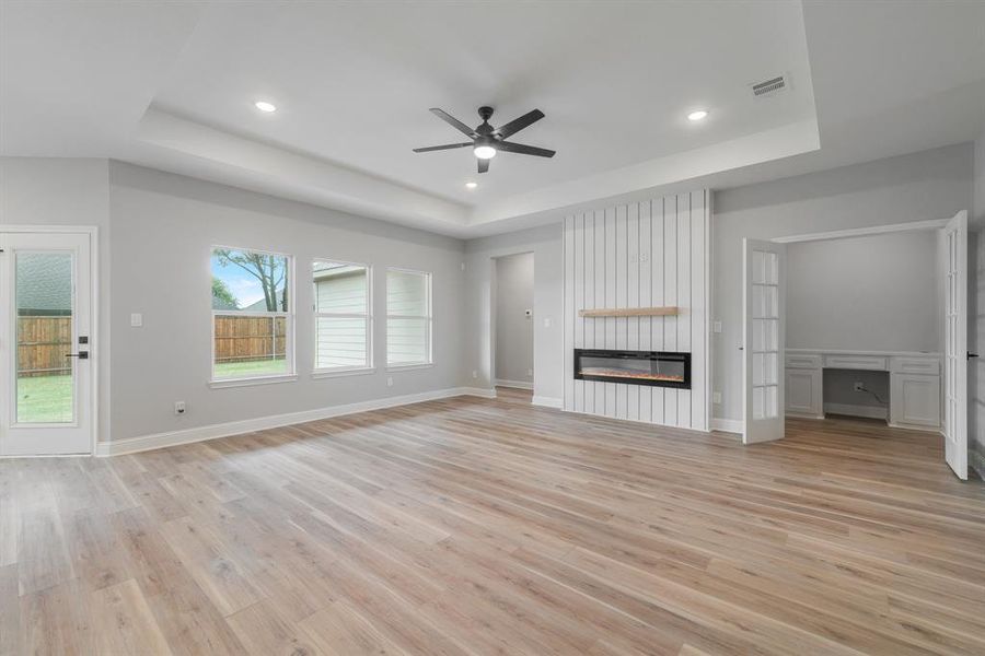 Unfurnished living room with a tray ceiling, a large fireplace, light wood-type flooring, and ceiling fan