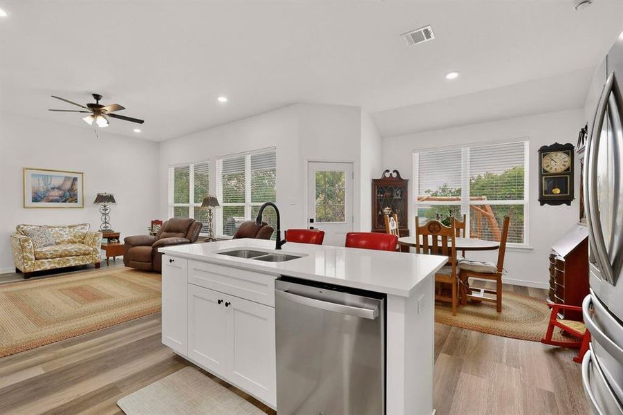Open-concept living space featuring a kitchen island with white cabinetry, a stainless steel dishwasher, and a double basin sink with a matte black faucet