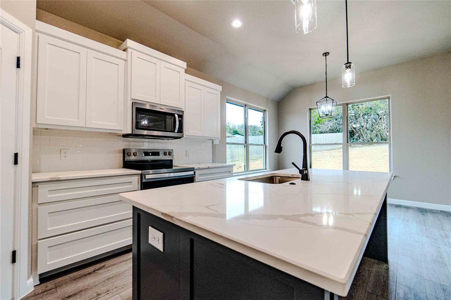 Kitchen with stainless steel appliances, a center island with sink, white cabinets, and decorative backsplash