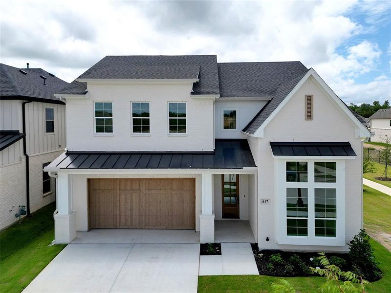 Modern inspired farmhouse featuring a standing seam roof, a shingled roof, driveway, an attached garage, and a front yard Modern inspired farmhouse featuring a standing seam roof, a shingled roof, driveway, an attached garage, and a front yard