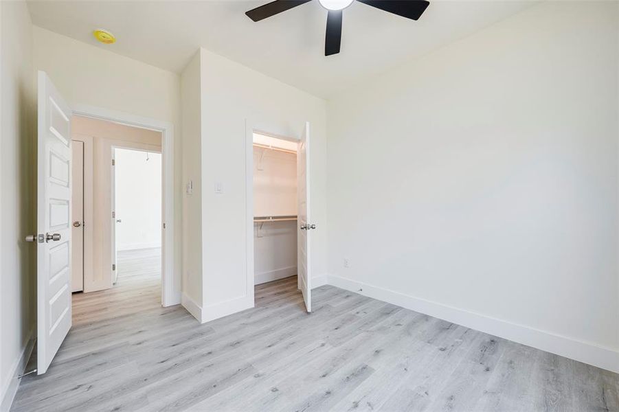 Bedroom with light wood-style flooring, a spacious closet, and a ceiling fan