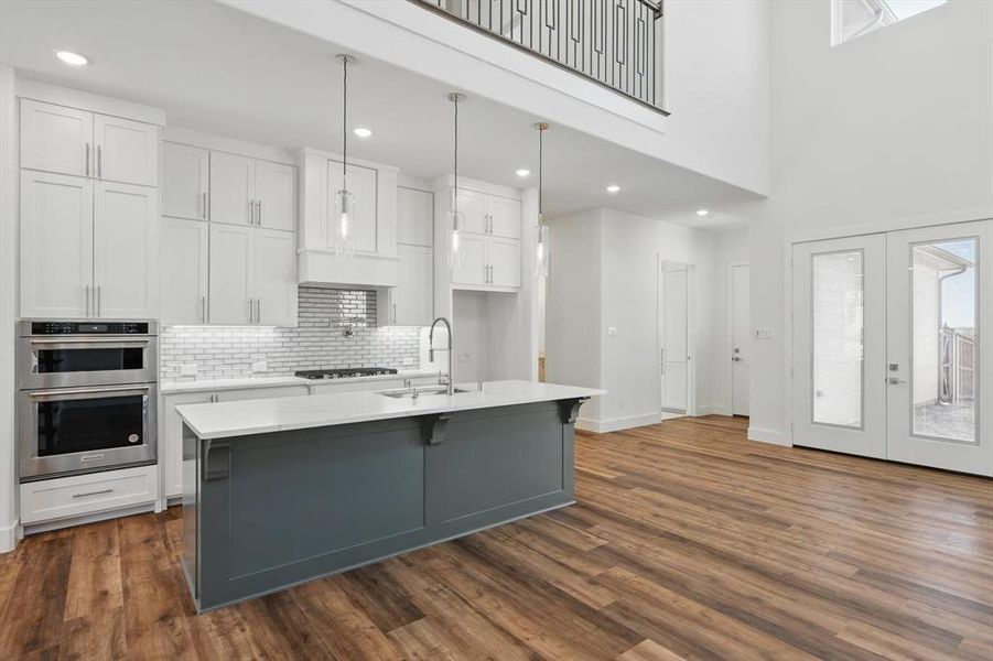 Kitchen with light countertops, appliances with stainless steel finishes, a kitchen island with sink, a sink, and white cabinetry