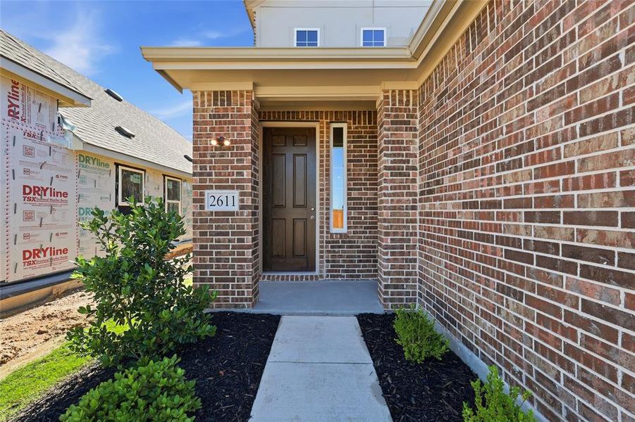 Brick exterior featuring a covered entry, dark wood-paneled door, vertical accent window, and concrete walkway