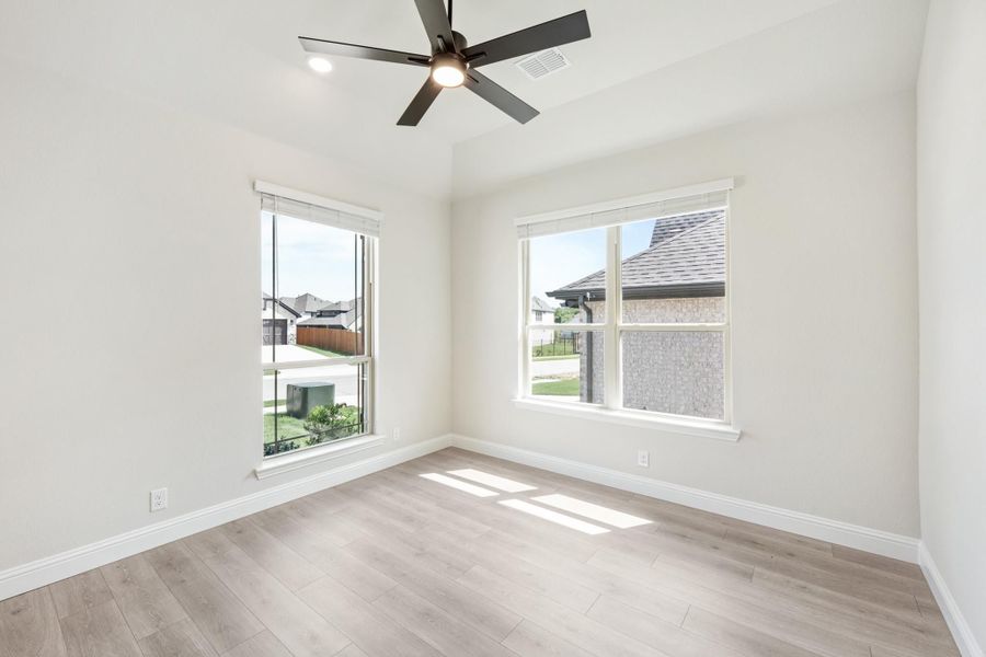 Empty bedroom with light wood floors, ceiling fan, and two windows with neighborhood views Empty bedroom with light wood floors, ceiling fan, and two windows with neighborhood views