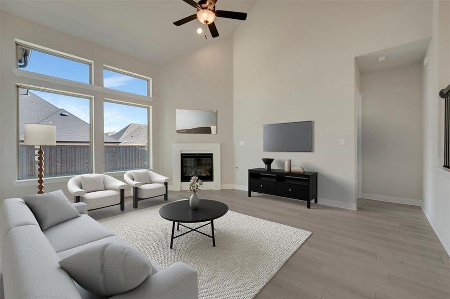 Living room featuring a glass covered fireplace, light wood finished floors, a ceiling fan, and lofted ceiling