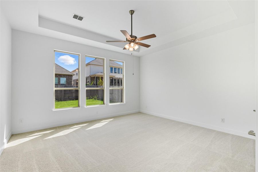 Empty room with a tray ceiling, light colored carpet, and a ceiling fan