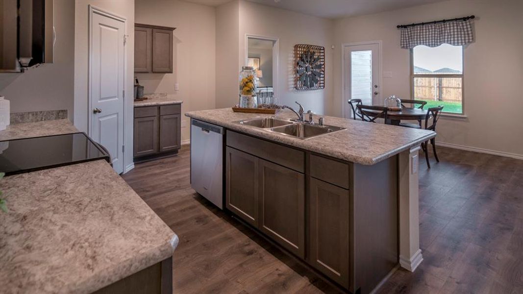 Kitchen featuring an island with double basin stainless steel sink, wood-finish flooring, and light-toned countertops