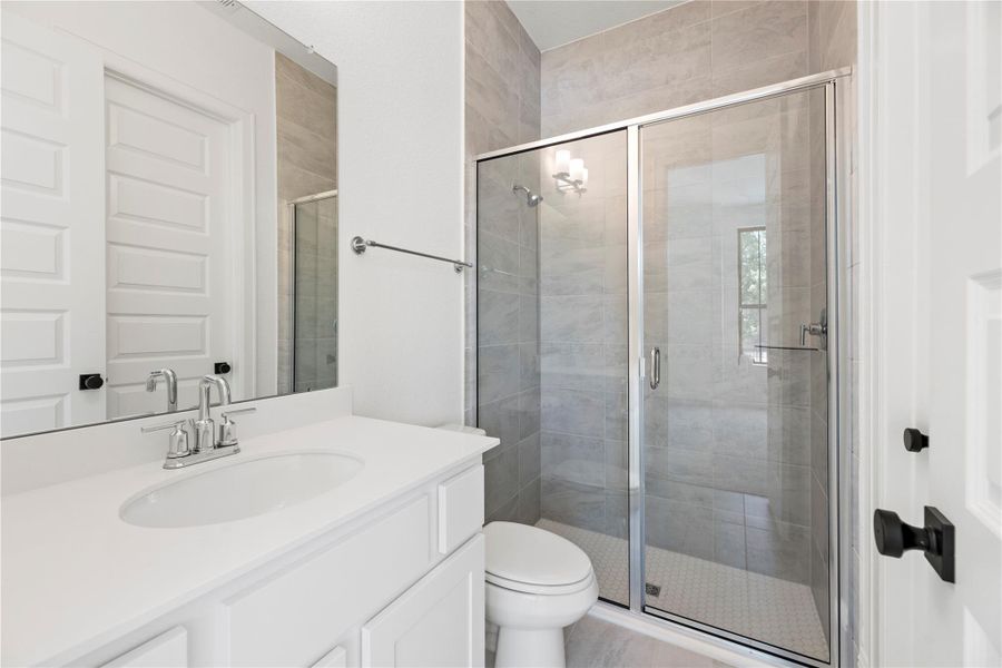 Secondary bathroom features a walk-in glass shower with modern tile surround and white cabinetry.