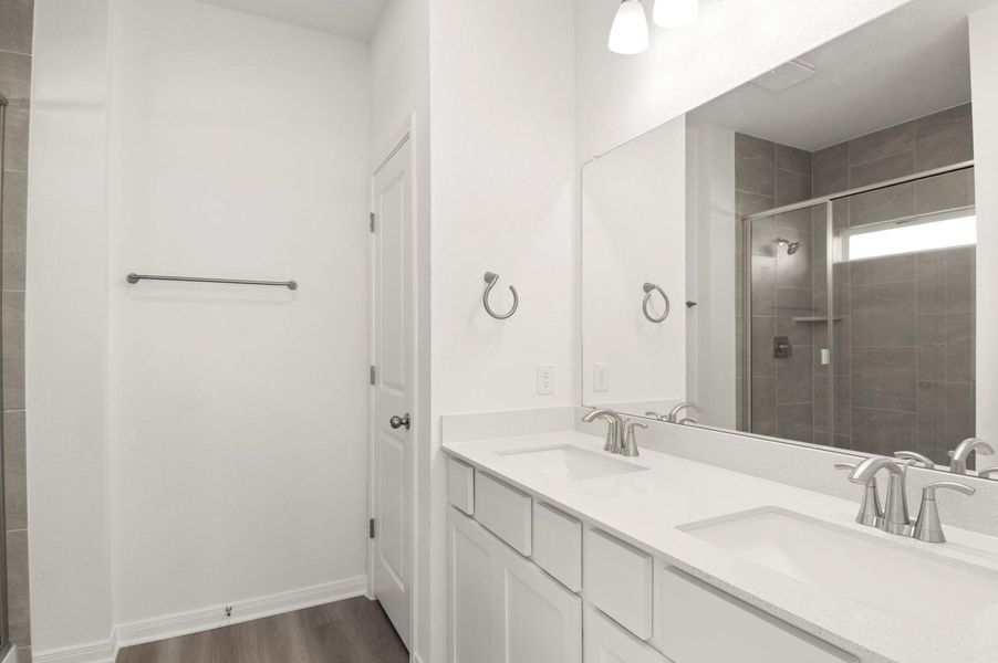 Bathroom featuring a shower stall, double vanity, and dark wood-style floors