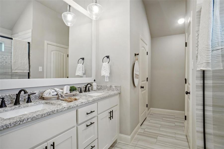 Bathroom with double sink vanity, tile patterned flooring, and lofted ceiling