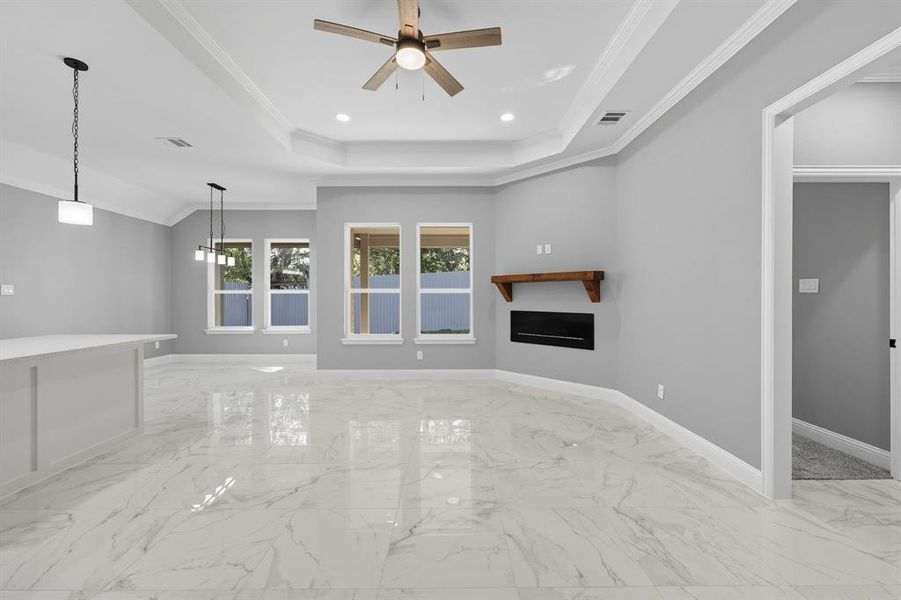 Unfurnished living room featuring a fireplace, crown molding, light marble finish flooring, recessed lighting, and a raised ceiling Unfurnished living room featuring a fireplace, crown molding, light marble finish flooring, recessed lighting, and a raised ceiling