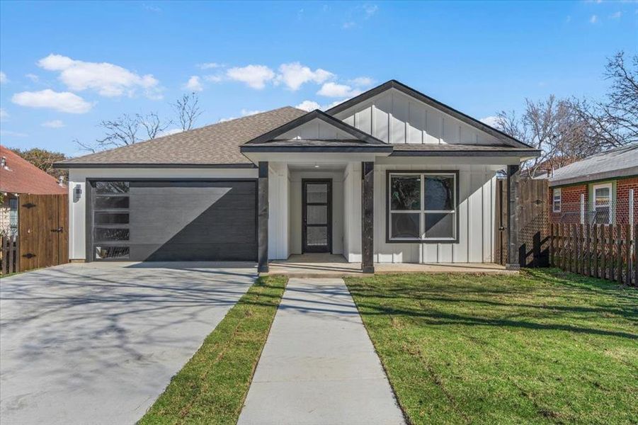 View of front of house featuring driveway, a garage, fence, board and batten siding, and a front yard