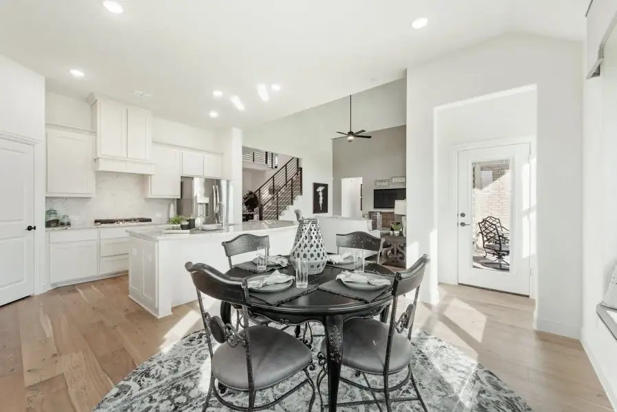 Open-concept dining area with round black table, hardwood floors, and white kitchen in background