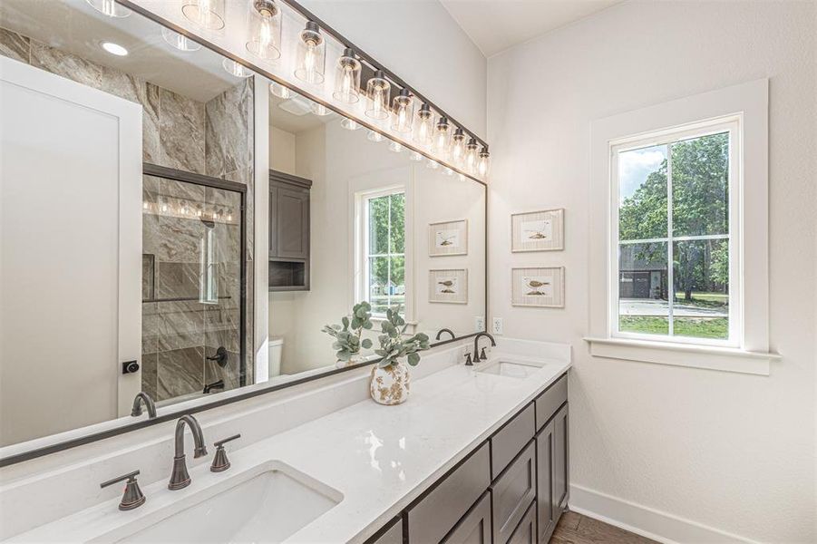 Bathroom featuring double vanity, tiled shower, and wood finished floors