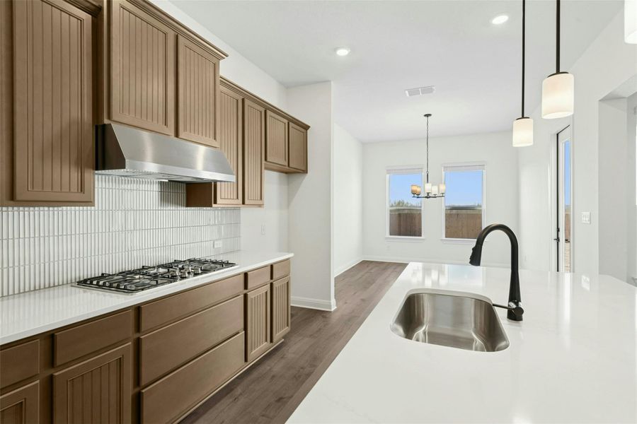 Kitchen with dark wood finished floors, decorative backsplash, suspended lighting, stainless steel gas cooktop, and light stone counters
