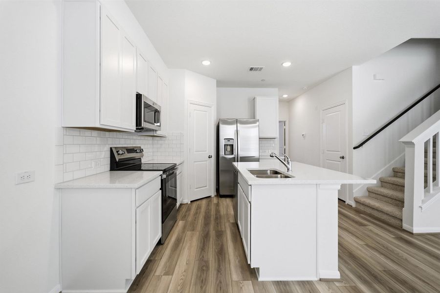 Kitchen with stainless steel appliances, white cabinetry, decorative backsplash, an island with sink, and recessed lighting Kitchen with stainless steel appliances, white cabinetry, decorative backsplash, an island with sink, and recessed lighting