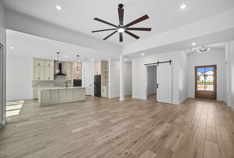 Unfurnished living room with a barn door, recessed lighting, light wood-style floors, ceiling fan, and a chandelier Unfurnished living room with a barn door, recessed lighting, light wood-style floors, ceiling fan, and a chandelier