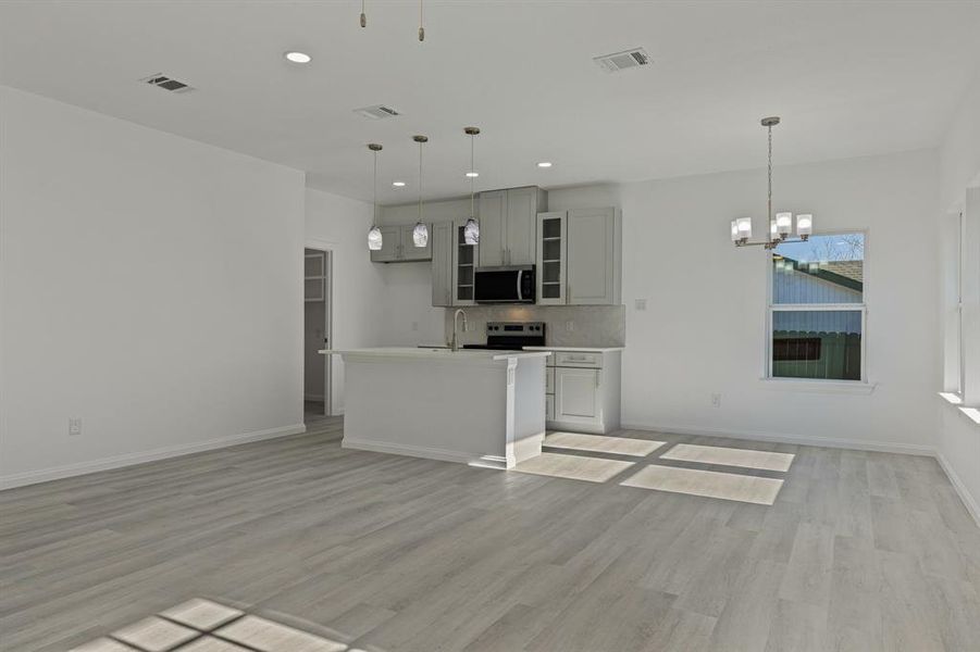 Kitchen with open floor plan, a chandelier, stainless steel appliances, hanging light fixtures, and light wood finished floors