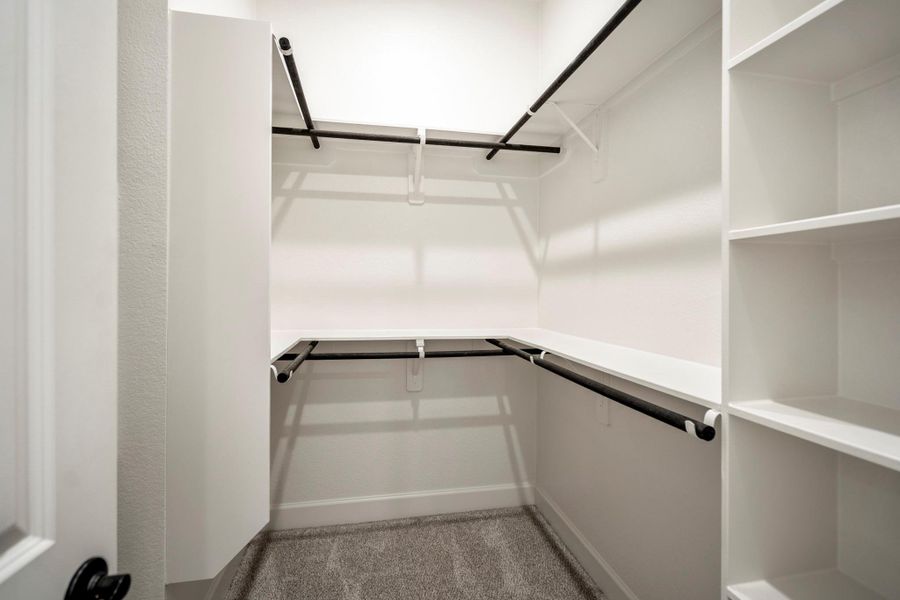 One of two spacious walk-in closets with multiple hanging rods and built-in shelves in the primary bedroom.