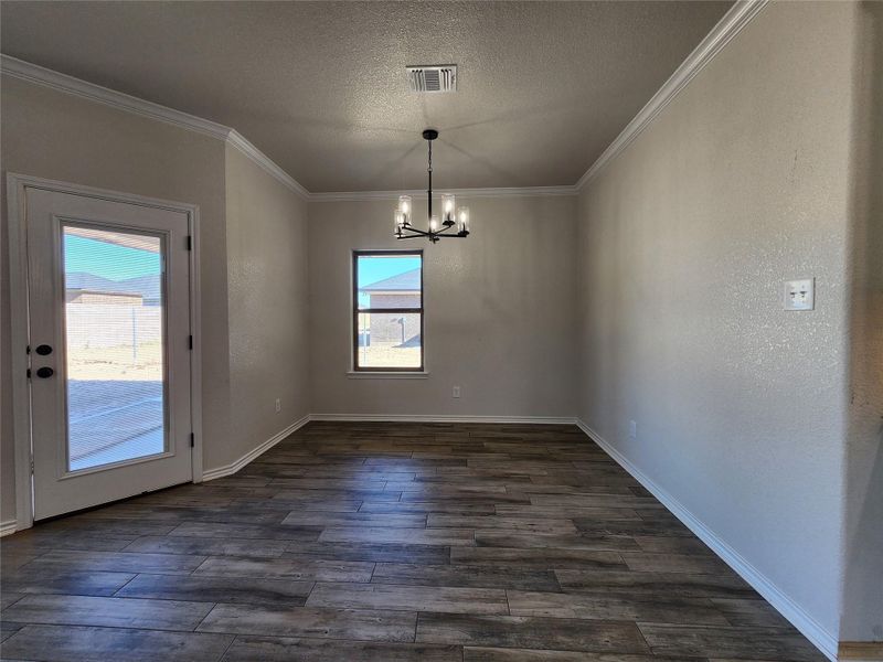 Unfurnished dining area with a textured ceiling, a chandelier, dark wood-type flooring, a textured wall, and plenty of natural light