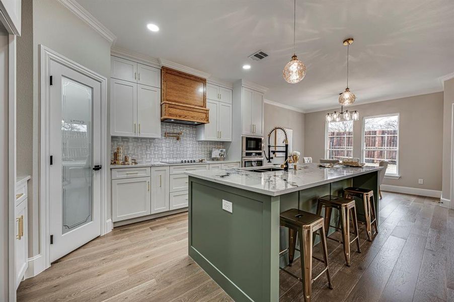 Kitchen featuring white cabinetry, hanging light fixtures, sink, and a center island with sink