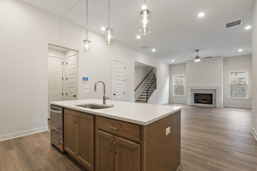 Kitchen island with integrated sink, wood-finish flooring, recessed lighting, and a fireplace with a mantel Kitchen island with integrated sink, wood-finish flooring, recessed lighting, and a fireplace with a mantel