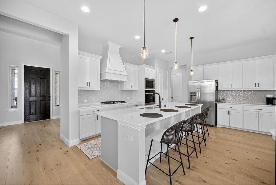 Bright kitchen featuring an expansive center island with seating, white shaker cabinetry, quartz countertops, and a herringbone tile backsplash