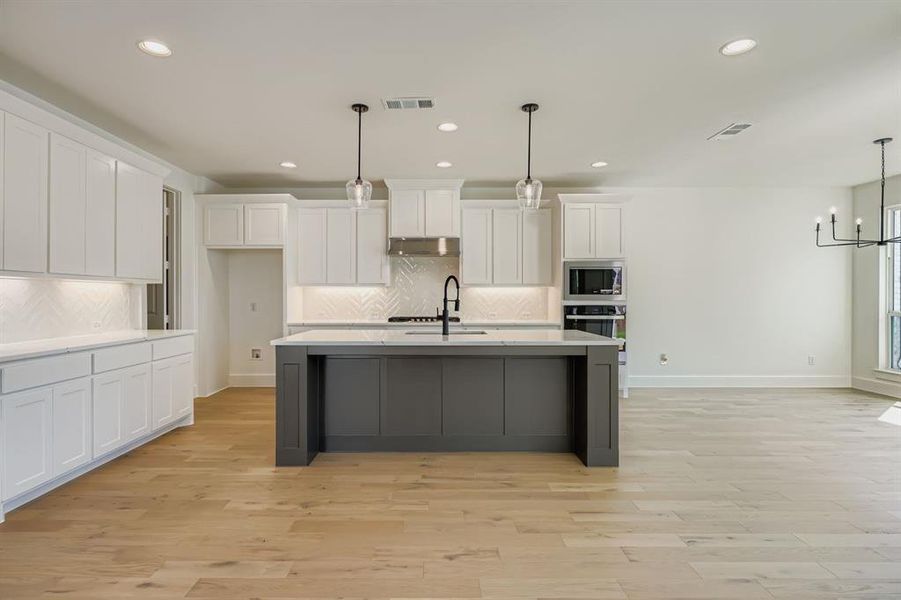 Kitchen featuring white cabinets, hanging light fixtures, light wood finished floors, decorative backsplash, and recessed lighting