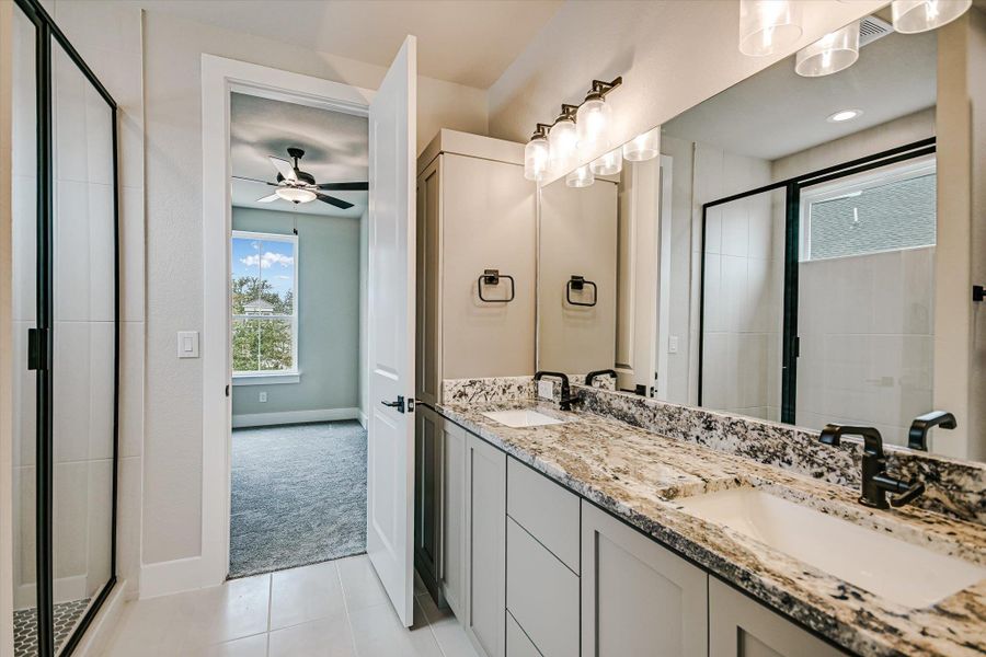 Full bath featuring a stall shower, double vanity, light carpet, light tile patterned floors, and ceiling fan