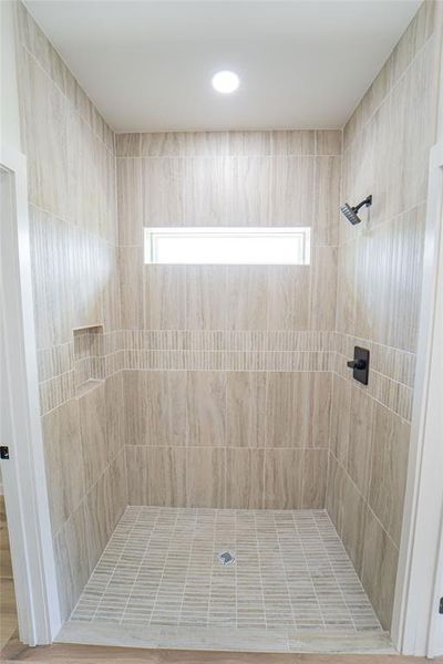Walk-in shower with vertical tile detailing, a horizontal accent tile band, and a recessed niche