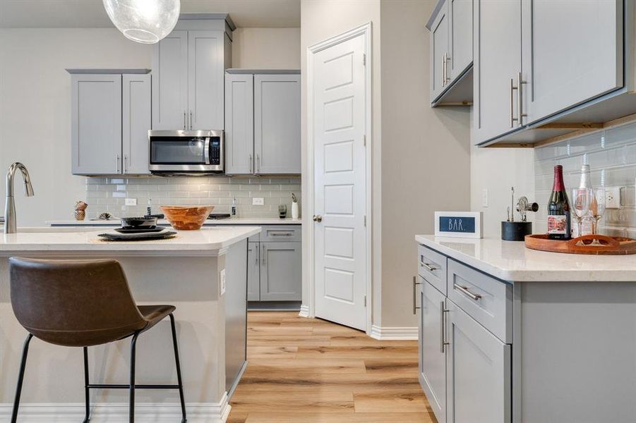 Kitchen with decorative backsplash, light wood-type flooring, gray cabinetry, and hanging light fixtures