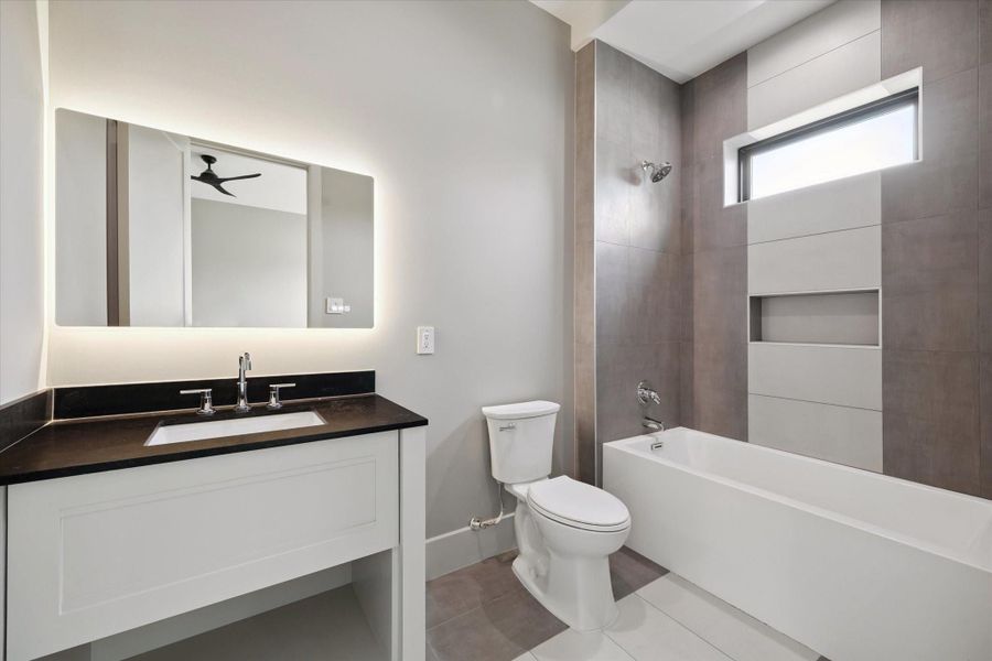 En-suite secondary bath features a quartz vanity with undermount sink and a lighted mirror for a refined touch. A tub/shower combination with a built-in soap inset makes it both practical and versatile for everyday living.