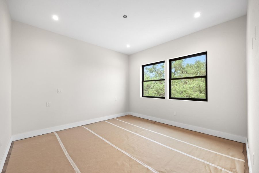 Recessed lighting illuminates this bright room featuring two windows with black frames and white baseboards