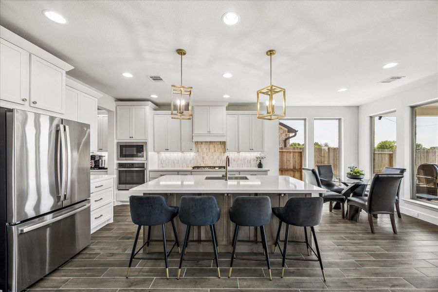 Chef's kitchen featuring a large quartz island, stainless steel appliances, custom cabinetry and designer pendant lighting