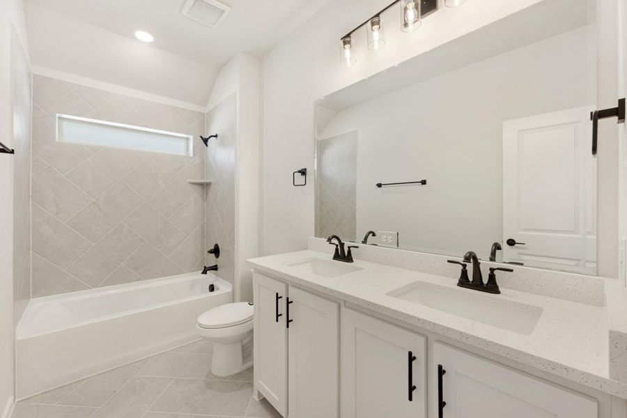 Bathroom with double sink vanity, white cabinets, tiled tub-shower combo, and black hardware fixtures