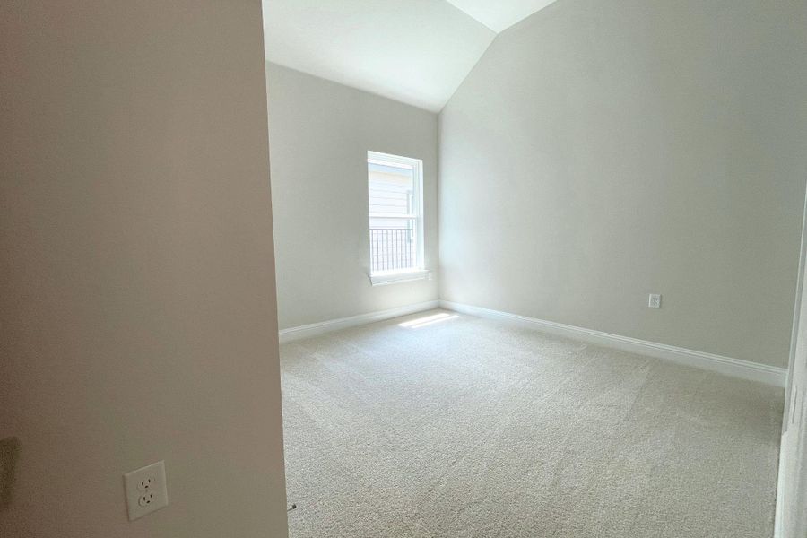 A well-lit, neutral-toned room features high vaulted ceilings and plush carpeting.