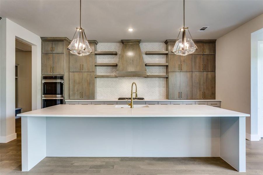 Kitchen featuring decorative backsplash, open shelves, a spacious island, premium range hood, and light wood finished floors Kitchen featuring decorative backsplash, open shelves, a spacious island, premium range hood, and light wood finished floors