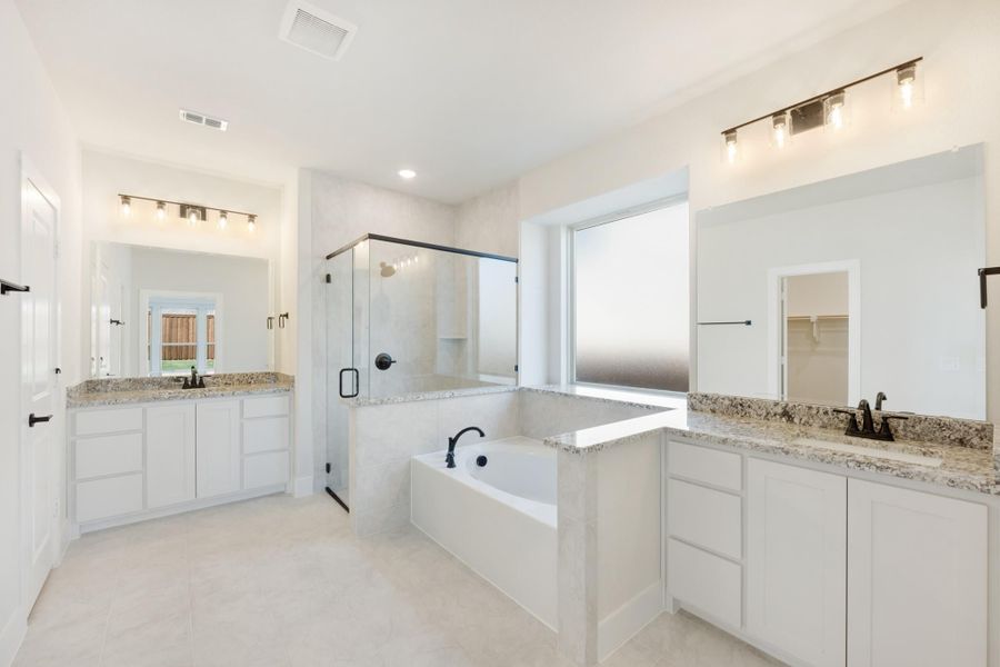 Master bathroom with dual vanities, soaking tub, glass shower, and white cabinets with granite countertops