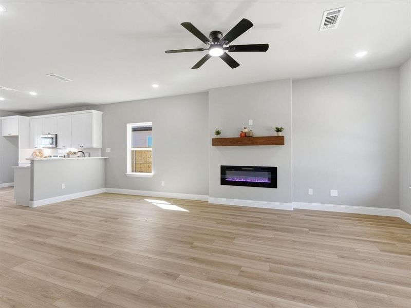 Unfurnished living room with light wood finished floors, recessed lighting, ceiling fan, and a glass covered fireplace Unfurnished living room with light wood finished floors, recessed lighting, ceiling fan, and a glass covered fireplace